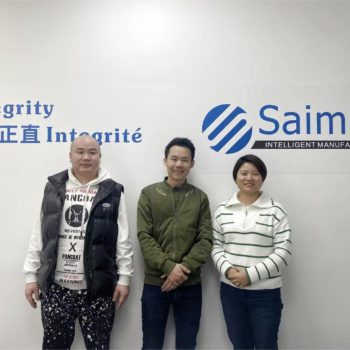 El equipo de Saimen con clientes visitantes frente a un muro que muestra el compromiso de la empresa con la integridad, destacando las asociaciones globales exitosas.