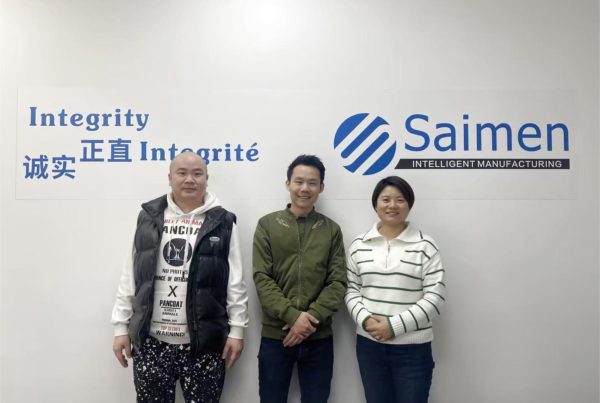 Saimen team with visiting clients in front of a wall showcasing the company’s commitment to integrity, highlighting successful global partnerships.
