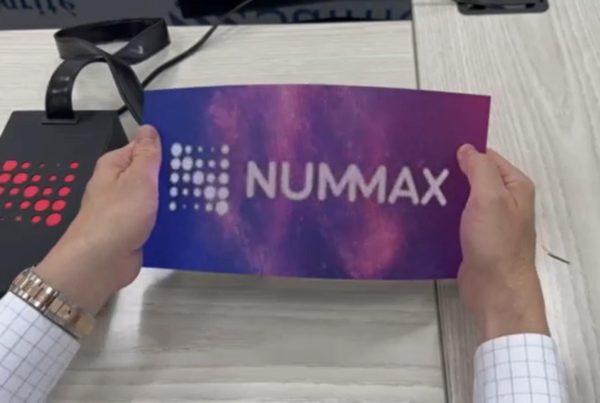 Hands presenting a NUMMAX brochure, featuring the new flexible DV-LED GOB thin high-resolution modules, showcasing cutting-edge display technology.