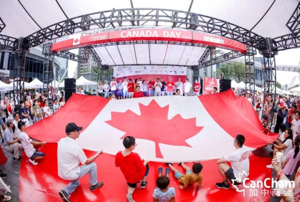 Crowd participating in a grand display of the Canadian flag at the CanCham Canada Day 2021 event in Shanghai, showcasing community spirit.